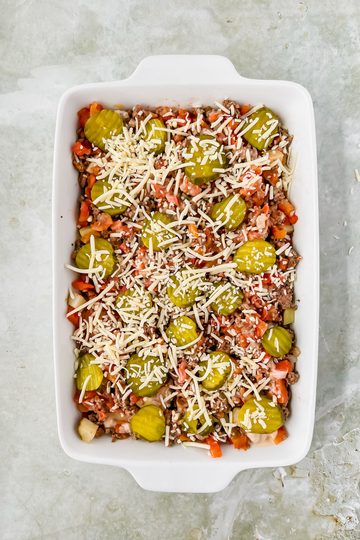 big mac casserole drizzled with fry sauce and topped with pickles and cheese prior to baking.