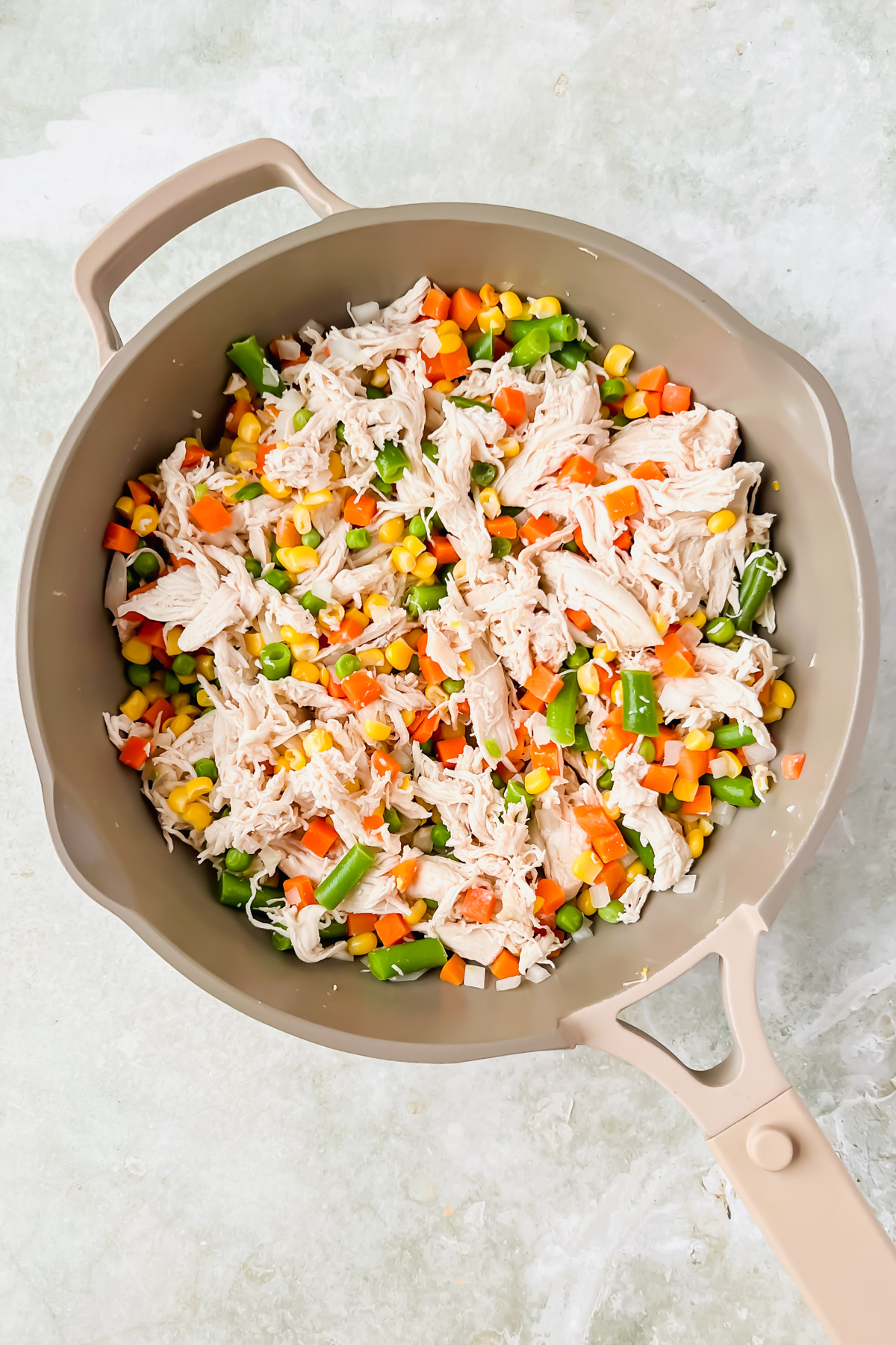 shredded chicken and mixed veggies in tan skillet.