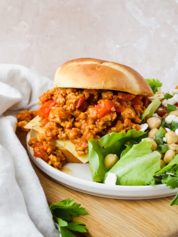 chicken sloppy joe beside mixed greens salad on white serving plate.