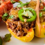 close up of enchilada stuffed bell peppers garnished with cilantro and jalapeño slice on white plate.