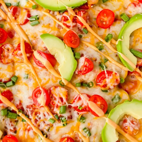 close up of baked healthy ground turkey enchiladas garnished with cherry tomato slices, avocado slices, green onion and queso.