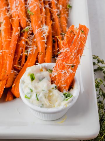 one carrot fry dipped into parmesan aioli on white plate with additional carrot fries.