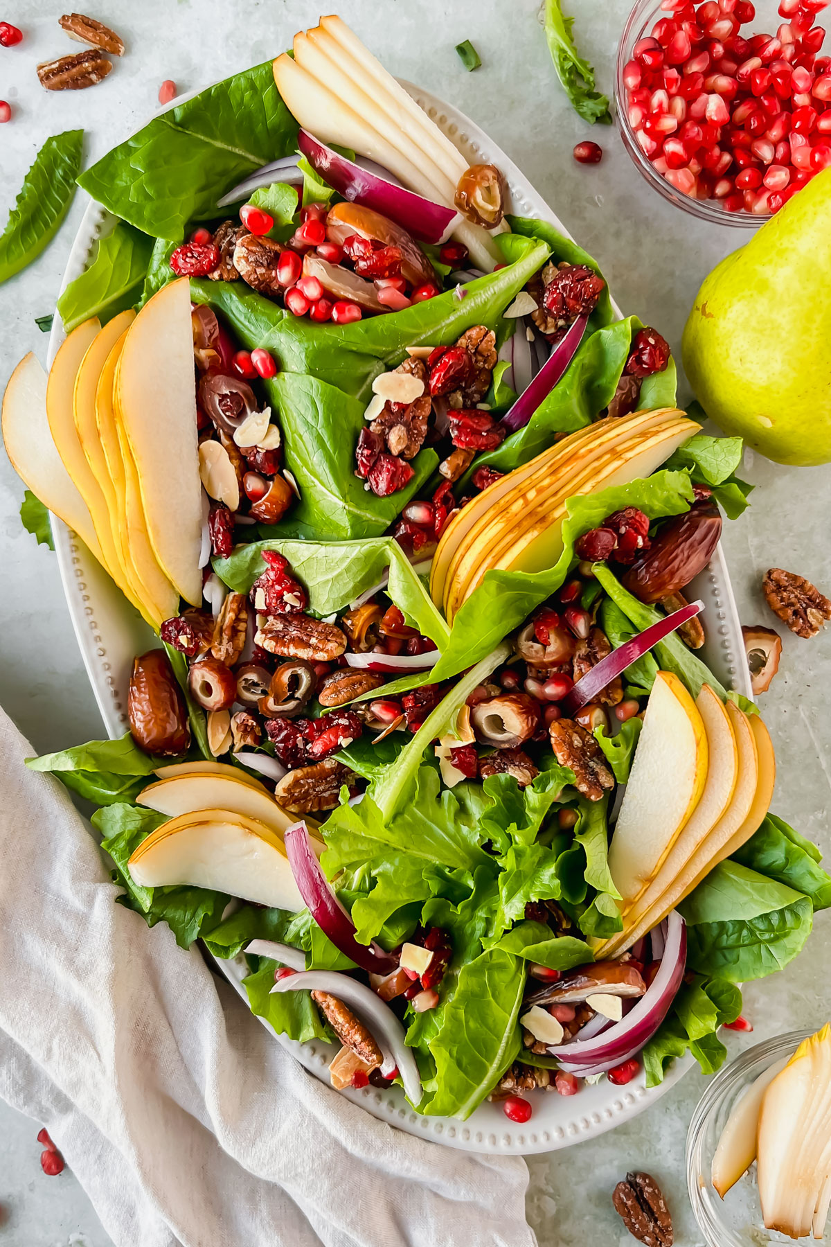 pear and pecan salad on white serving plate beside bowl of pomegranate seeds.