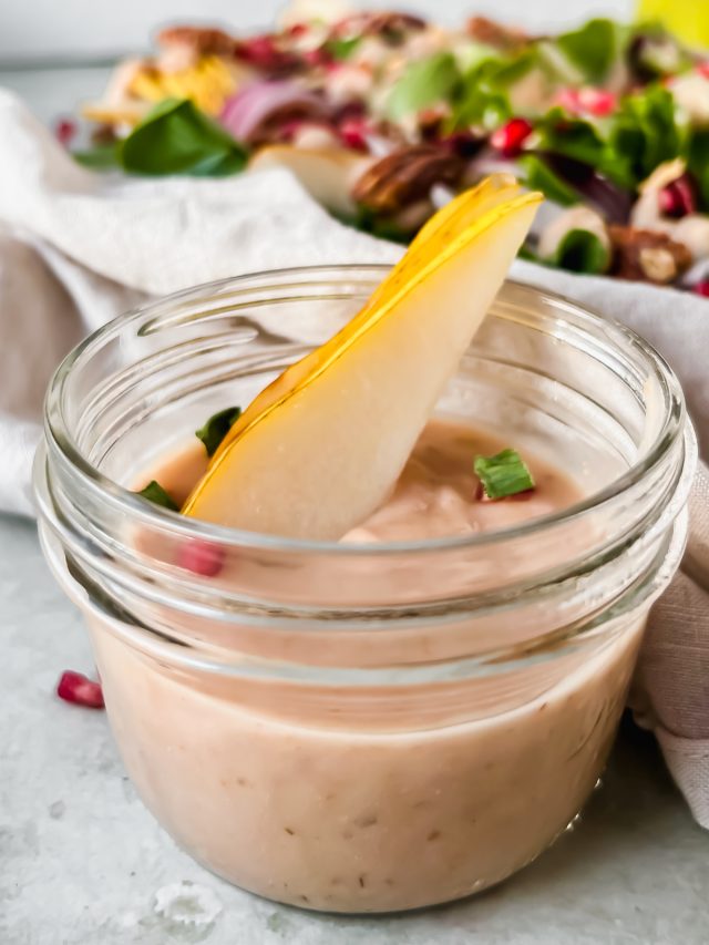 pear vinaigrette in small glass jar with pear and pecan salad in background.