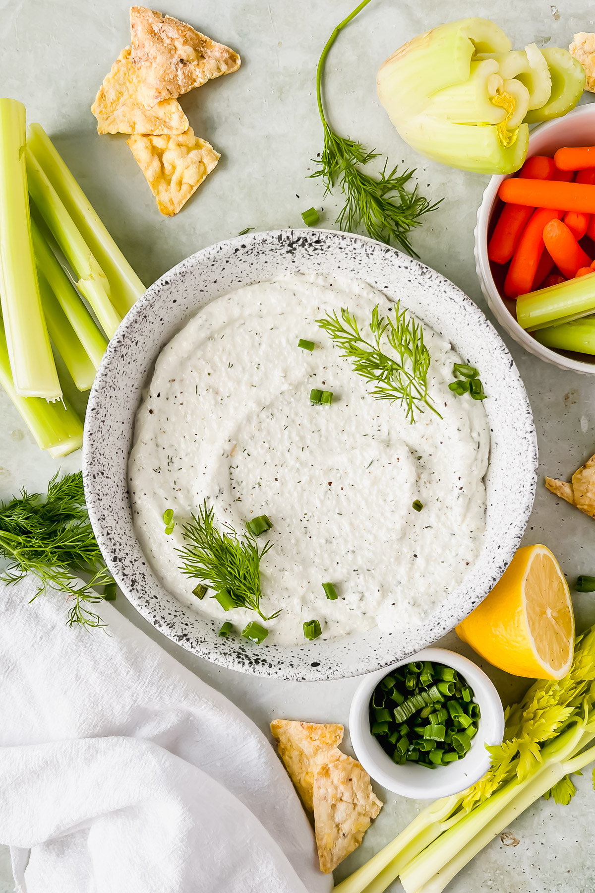 cottage cheese chip dip in speckled white bowl garnished with fresh dill and green onions with chips and vegetables surrounding bowl.