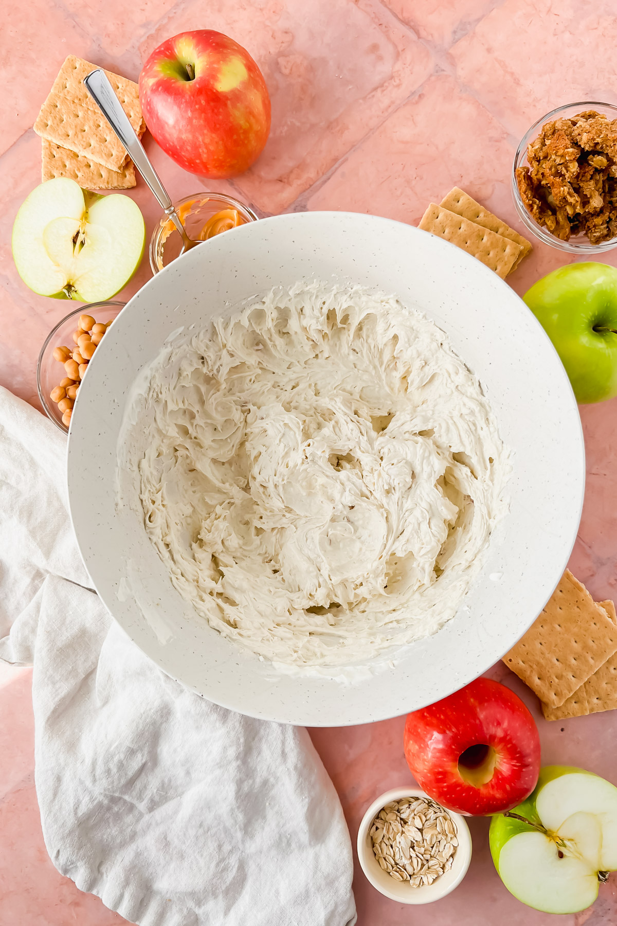 whipped cream cheese, yogurt, and cool whip in white mixing bowl surrounded by cream cheese caramel apple dip ingredients.