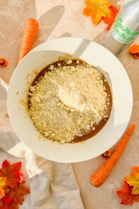raw carrot cake with pumpkin batter topped with dry ingredients in white mixing bowl.