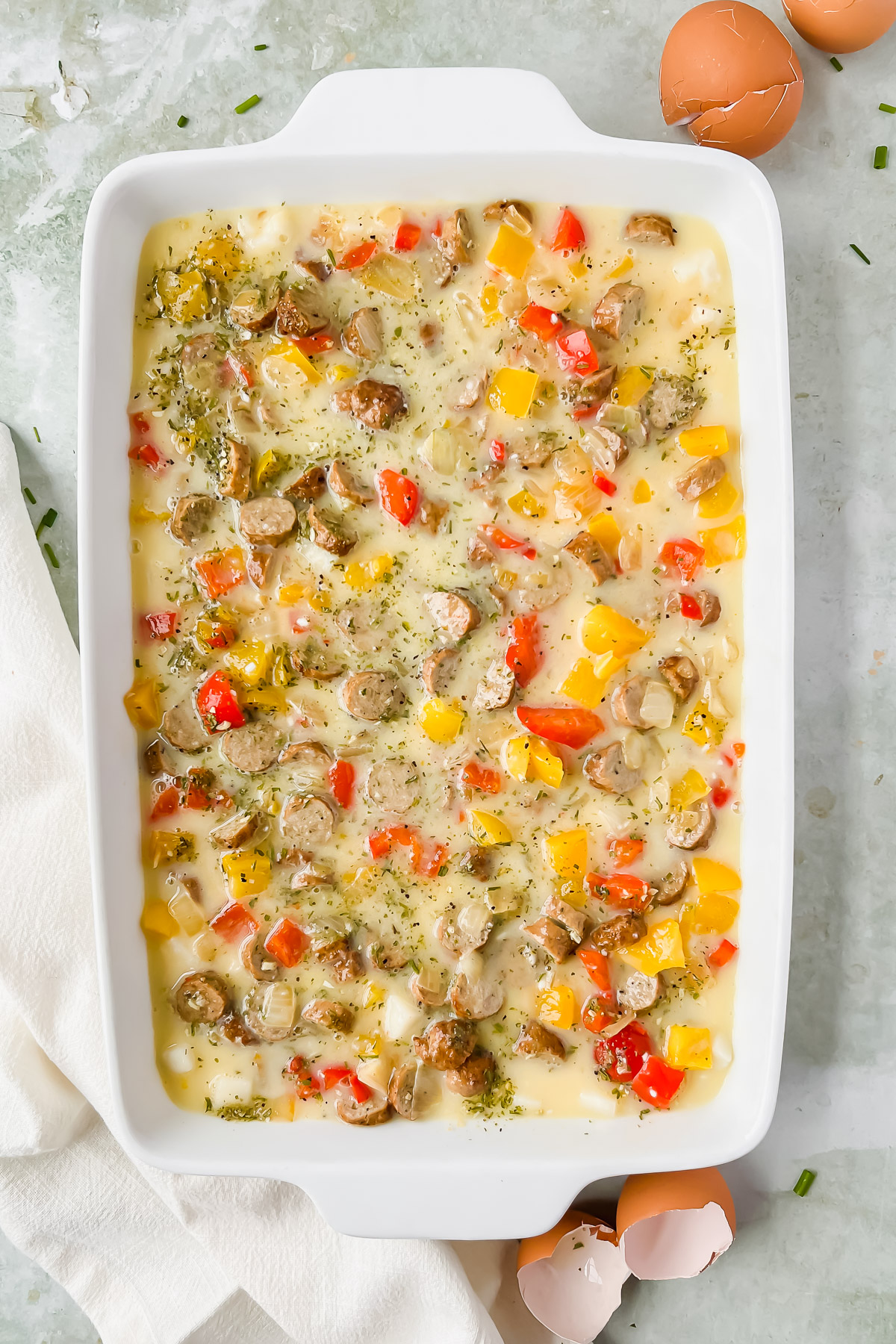 raw loaded hashbrown casserole topped with seasonings in white rectangular baking dish.
