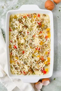 raw loaded hashbrown casserole topped with shredded cheese in white rectangular baking dish.