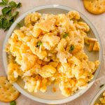 white plate full of lighter macaroni and cheese topped with crumbled ritz crackers surrounded by additional crackers and fresh herbs.