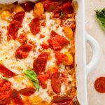 pizza gnocchi in white baking dish topped with pepperoni and basil leaves.