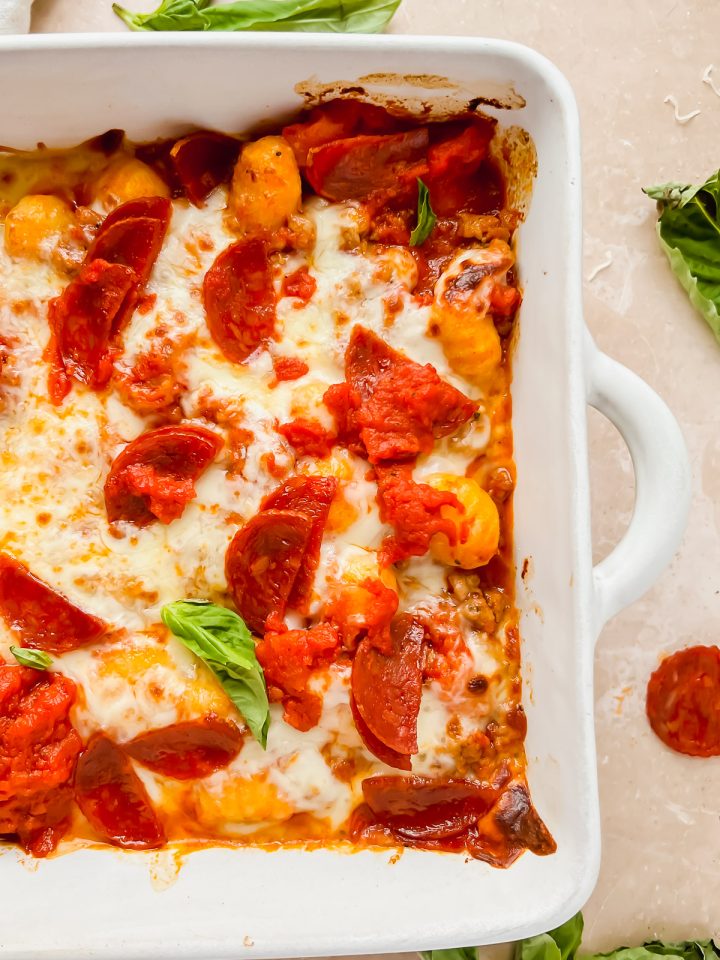 pizza gnocchi in white baking dish topped with pepperoni and basil leaves.