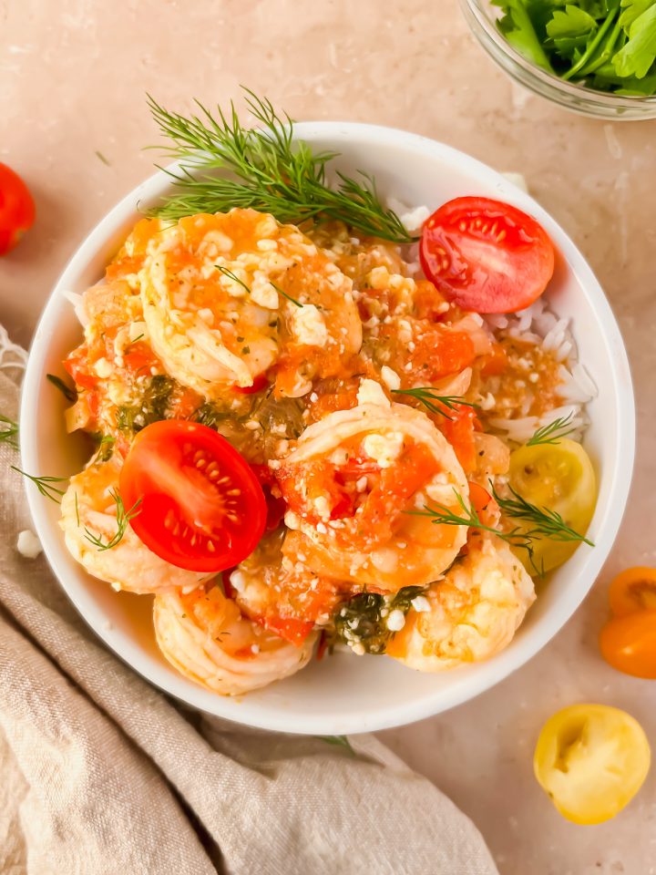 serving of shrimp saganaki garnished with fresh herbs and cherry tomato slices in white bowl.