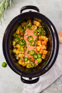 raw slow cooker pineapple pork topped with jalapeño slices in crock pot before cooking.