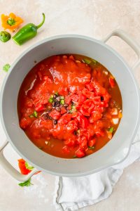 smokey bacon chili mixture with tomato sauce added on top in large gray soup pot.