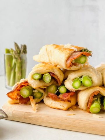 stacked asparagus in puff pastry with bacon on wood cutting board.