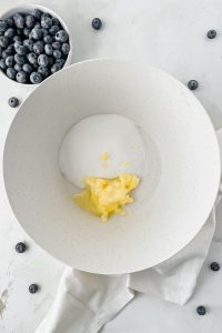 butter and sugar in white mixing bowl beside smaller bowl of fresh blueberries.