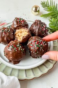 buckeye balls with rice krispies covered in chocolate and topped with christmas sprinkles with bite taken out of one to expose inside.