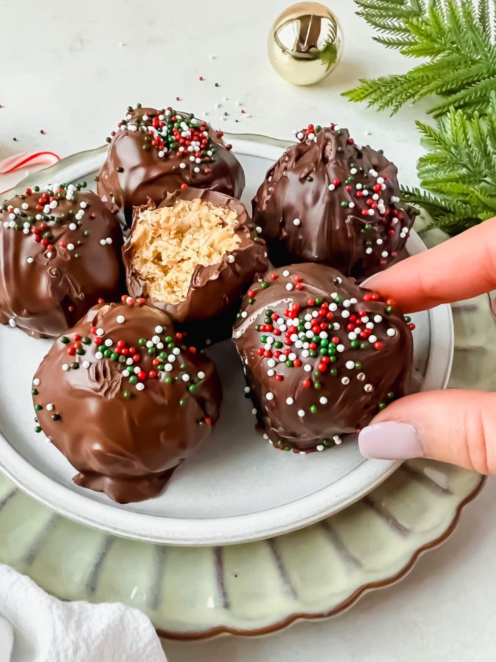 buckeye balls with rice krispies covered in chocolate and topped with christmas sprinkles with bite taken out of one to expose inside.