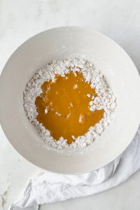 melted peanut butter poured over powdered sugar and rice krispies in white mixing bowl.