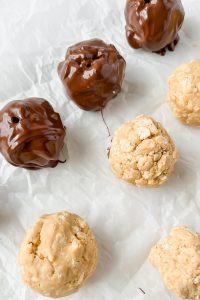 buckeye balls on white parchment paper half covered in chocolate.