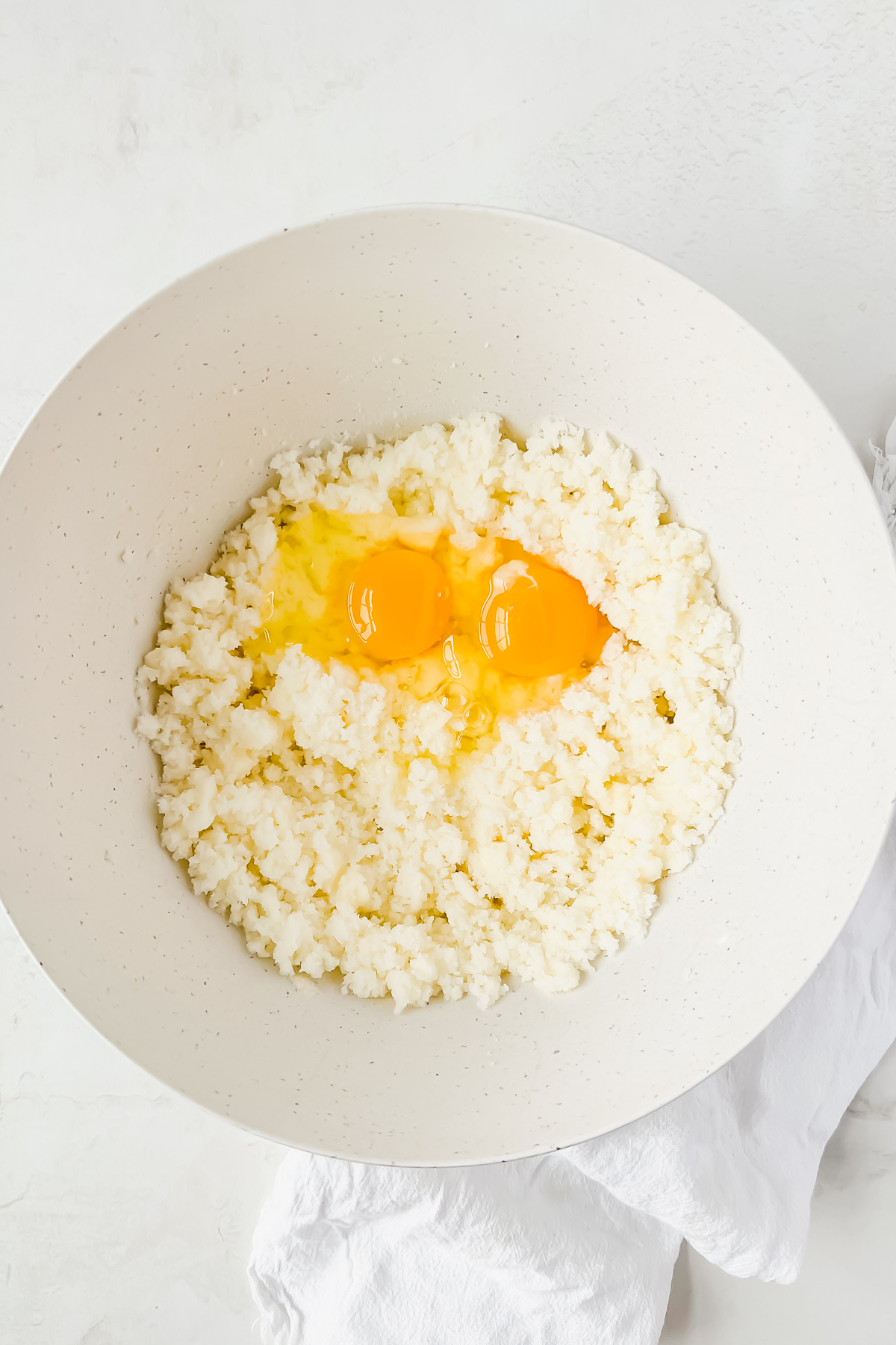 butter and sugar creamed in white mixing bowl with two eggs cracked into bowl.