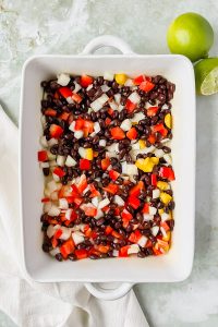black beans, red pepper, and white onion in greased white rectangular baking dish.