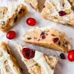 cranberry white chocolate bars drizzled with white chocolate cut into triangles on white parchment.