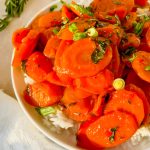 sweet and spicy carrots in white serving bowl over bed of rice garnished with fresh herbs.