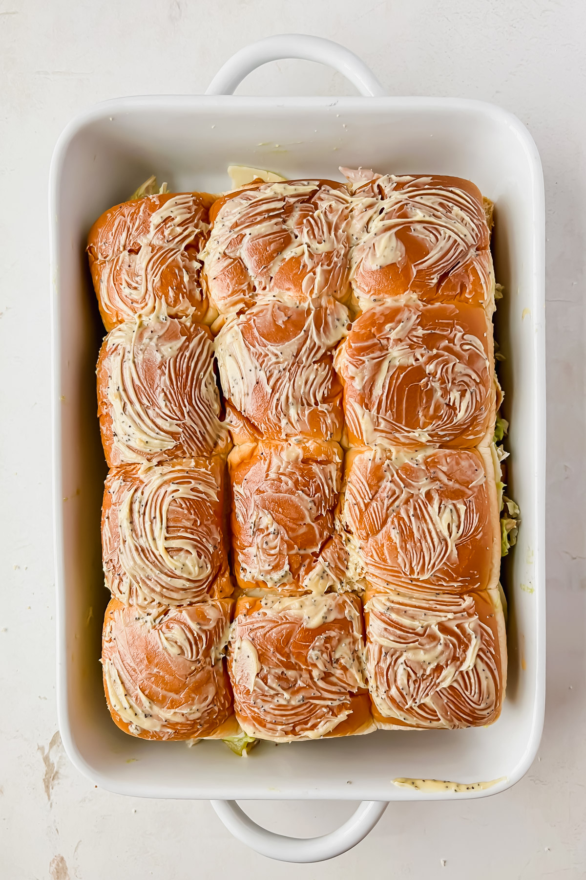 12 rotisserie chicken sliders in white baking dish topped with butter.
