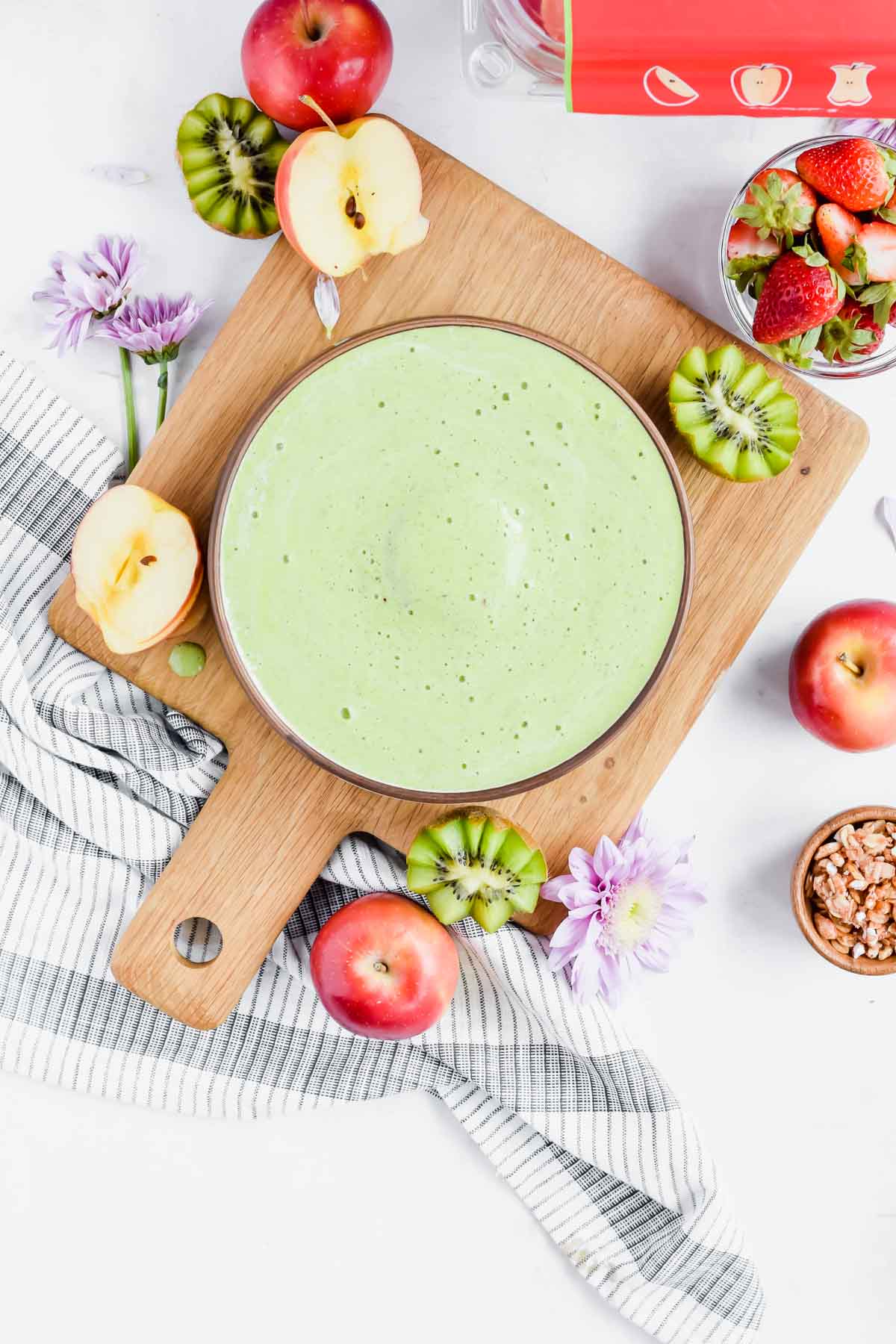 Apple Kiwi Smoothie in a bowl on a cutting board surrounded by fresh apples and kiwi.