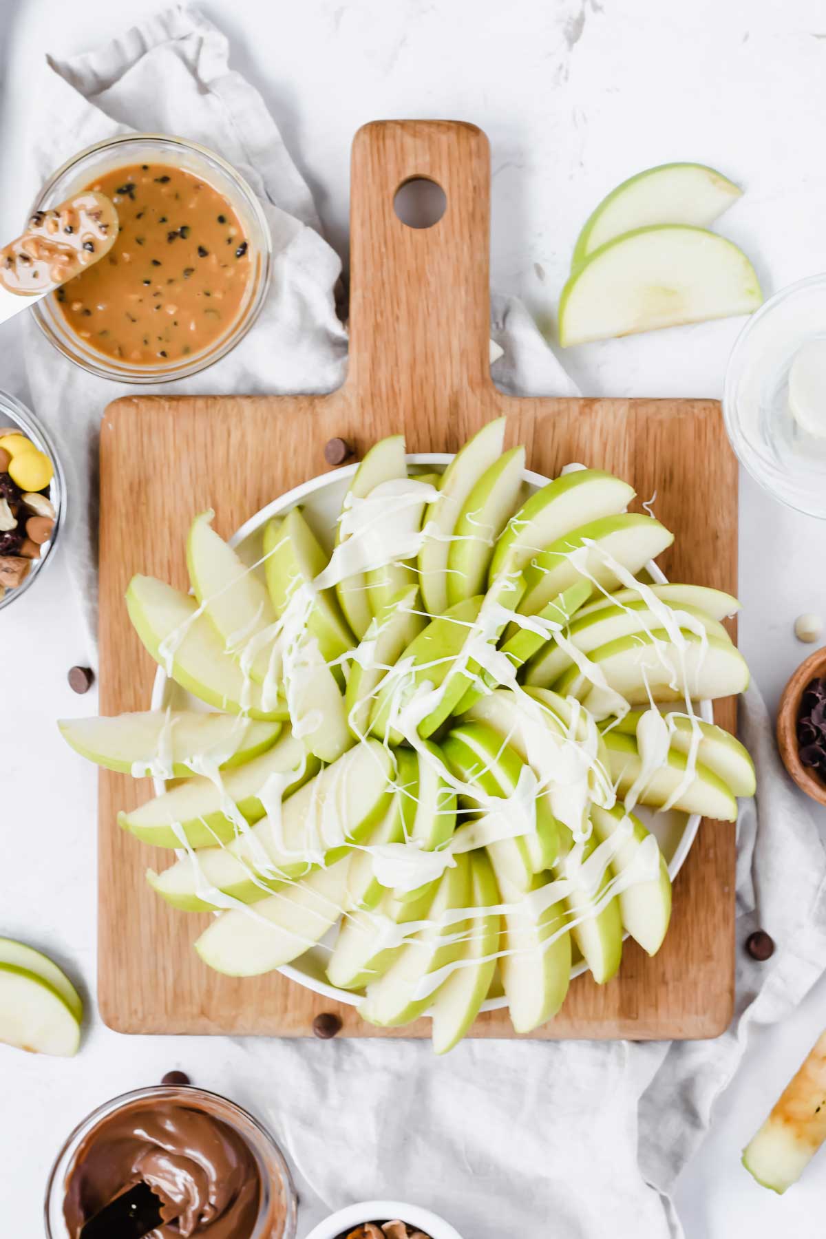 sliced apples arranged in circular fashion on wood cutting board surrounded by apple nacho ingredients.