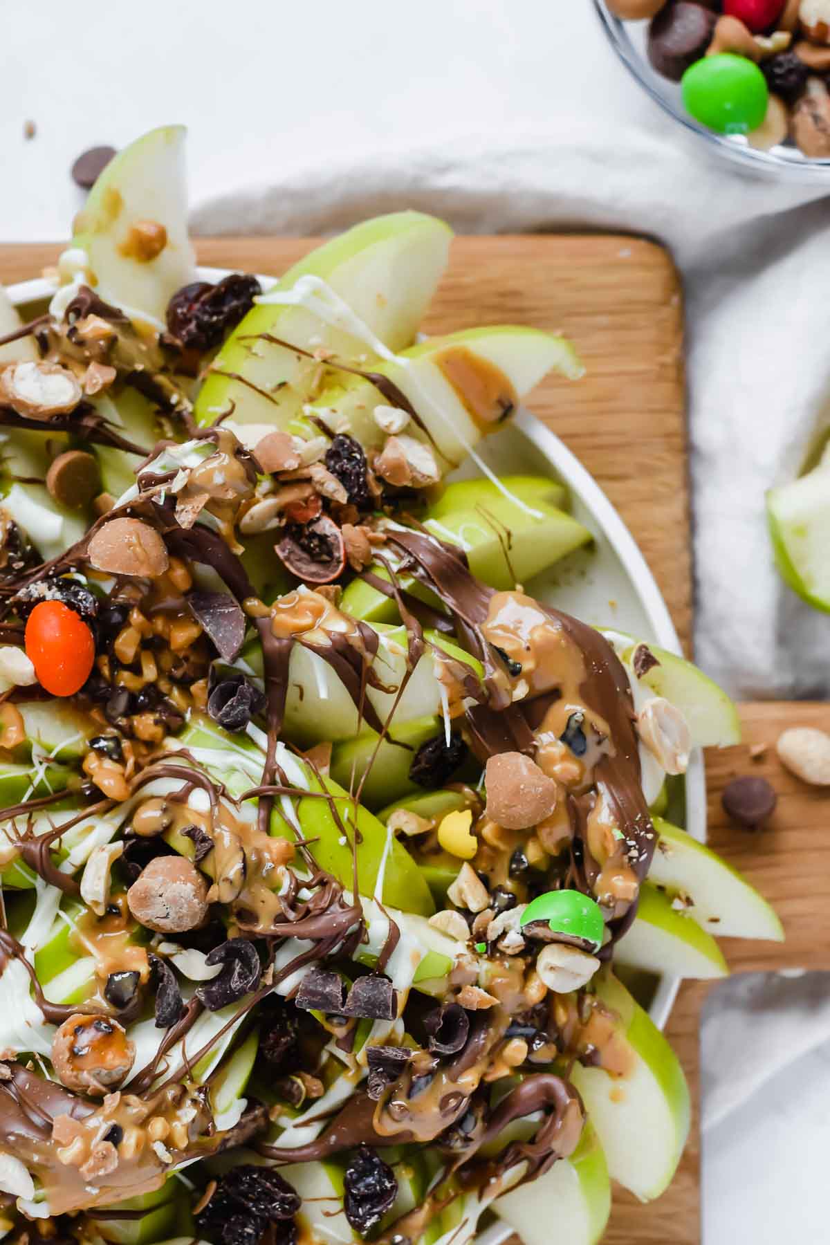 board full of apple nachos drizzled with chocolate and topped with trail mix.