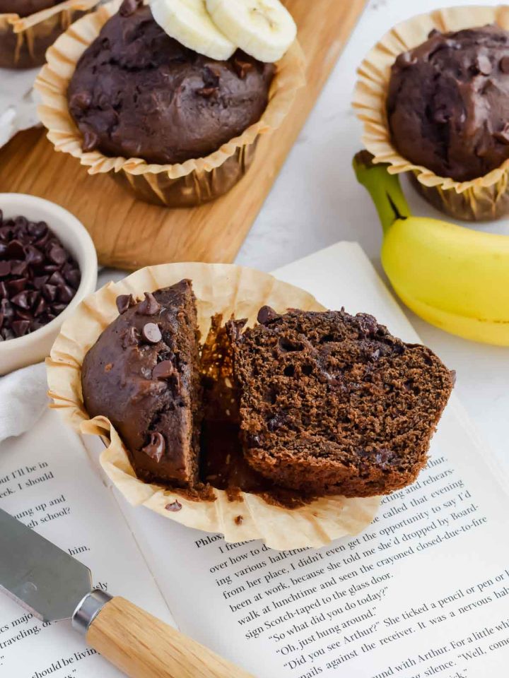 chocolate banana muffin cut in half on top of a book with other muffins in the background.
