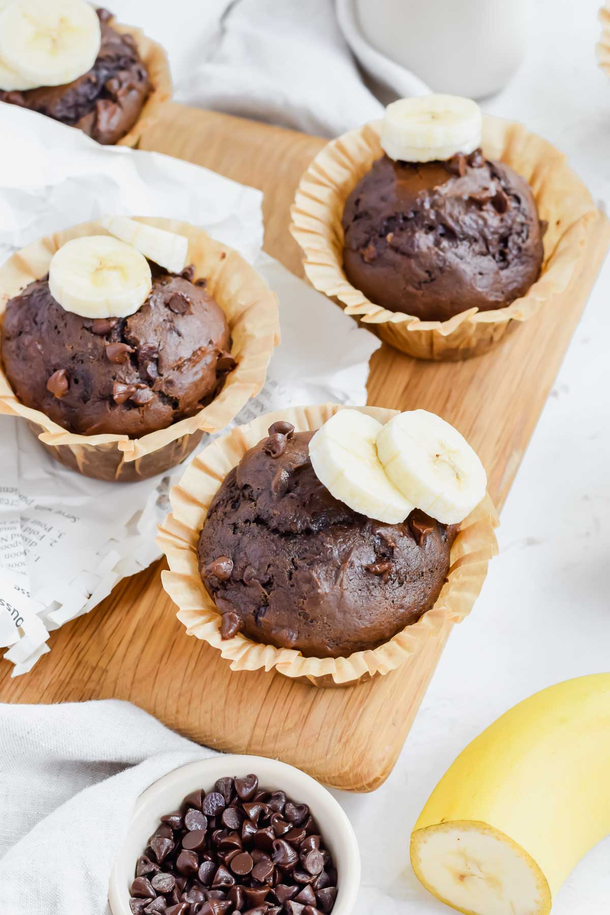 One Bowl Double Chocolate Banana Muffins topped with fresh banana slices on a wooden serving board.