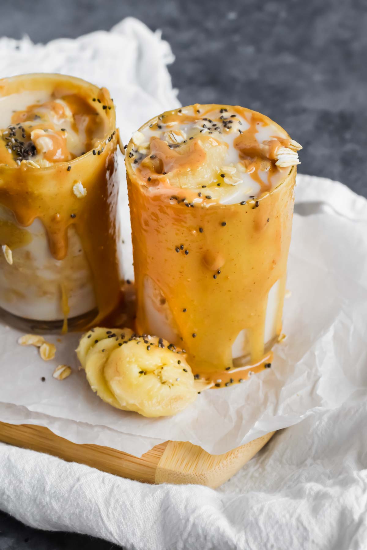 peanut butter overflowing on the side of a cup stuffed with banana overnight oats.
