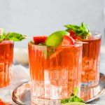 filled cocktail glasses with Caribbean Rum Punch topped with fresh mint, strawberries, and lime.