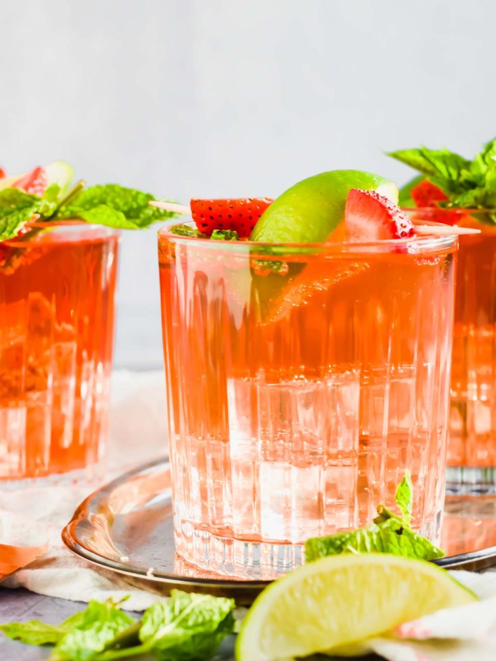 cocktail filled with ice and rum punch and garnished with strawberries and lime.