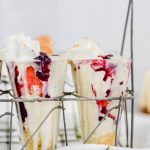 cheesecake milkshakes in glass cups, topped with whip cream and stacked with berries.