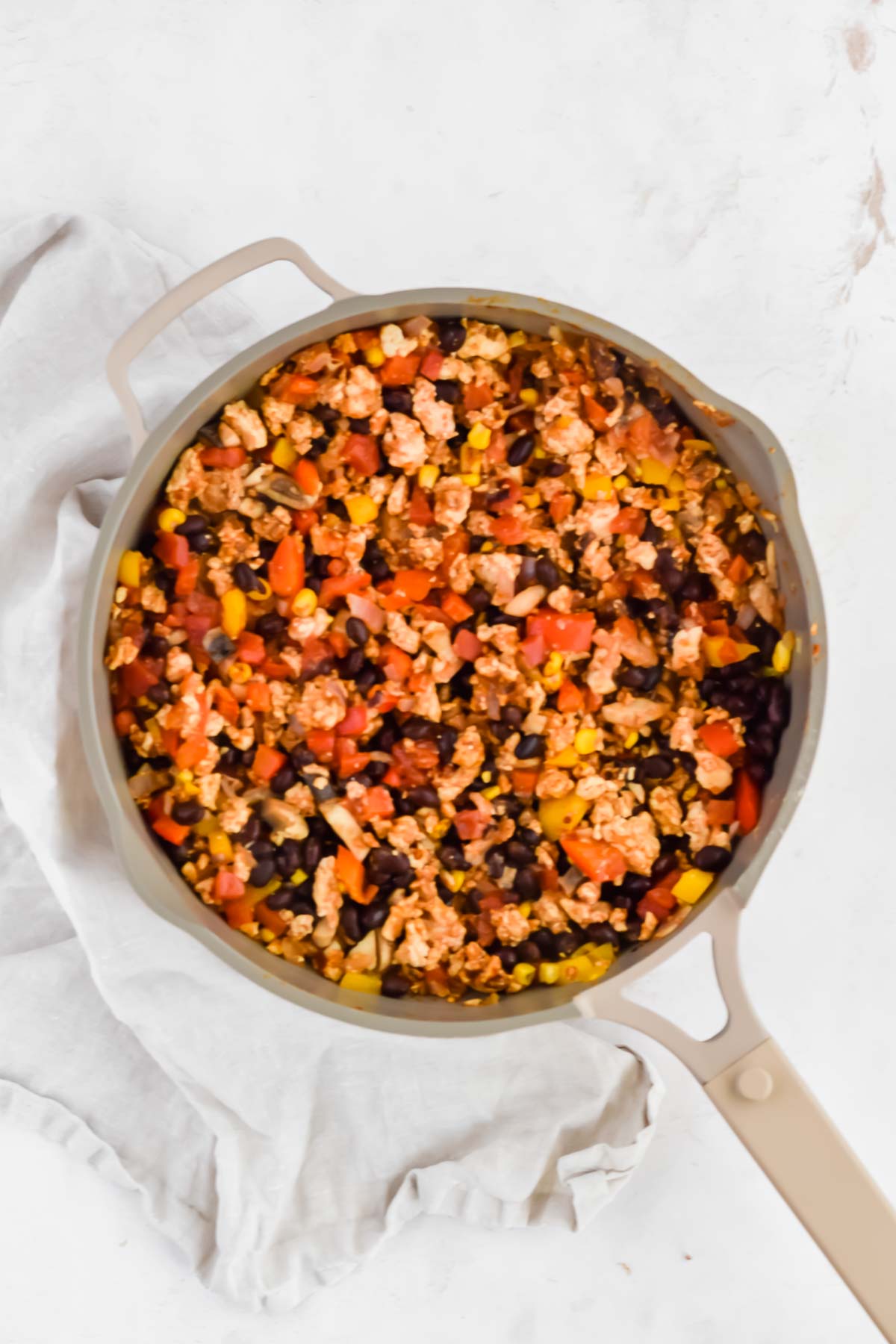 Ground chicken, black beans, bell peppers, and corn in a grey skillet.