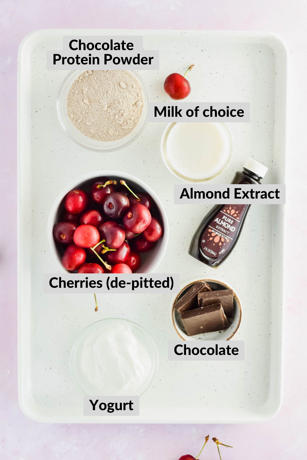 ingredients for chocolate cherry smoothie spread on white tray on light pink background.