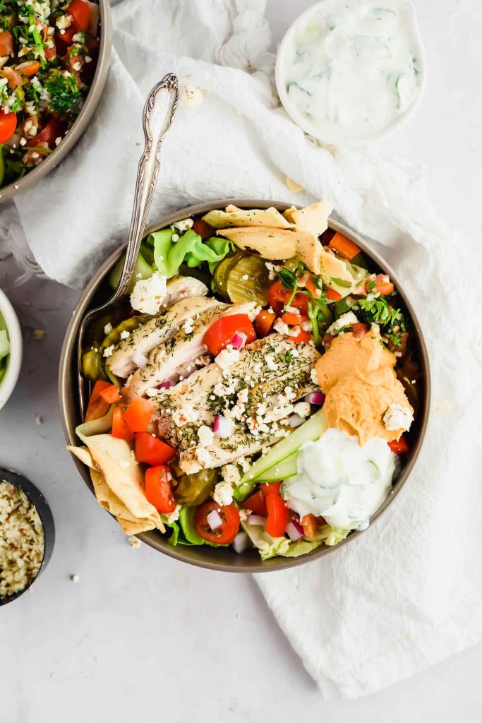 loaded Mediterranean salad with chicken, pita, tomatoes, red onions, pickles, hummus, tabbouleh, and tzatziki.