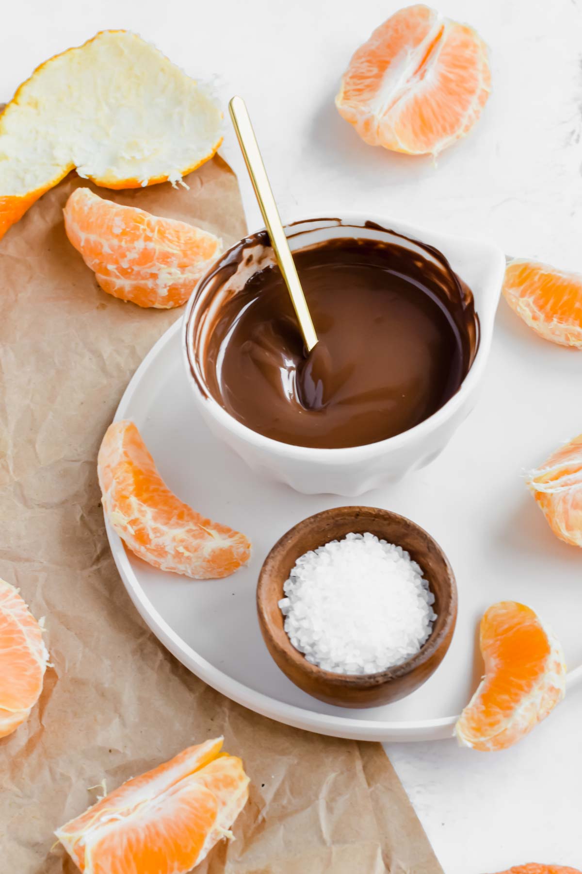 A plate with orange slices, sea salt, and melted chocolate in a bowl.
