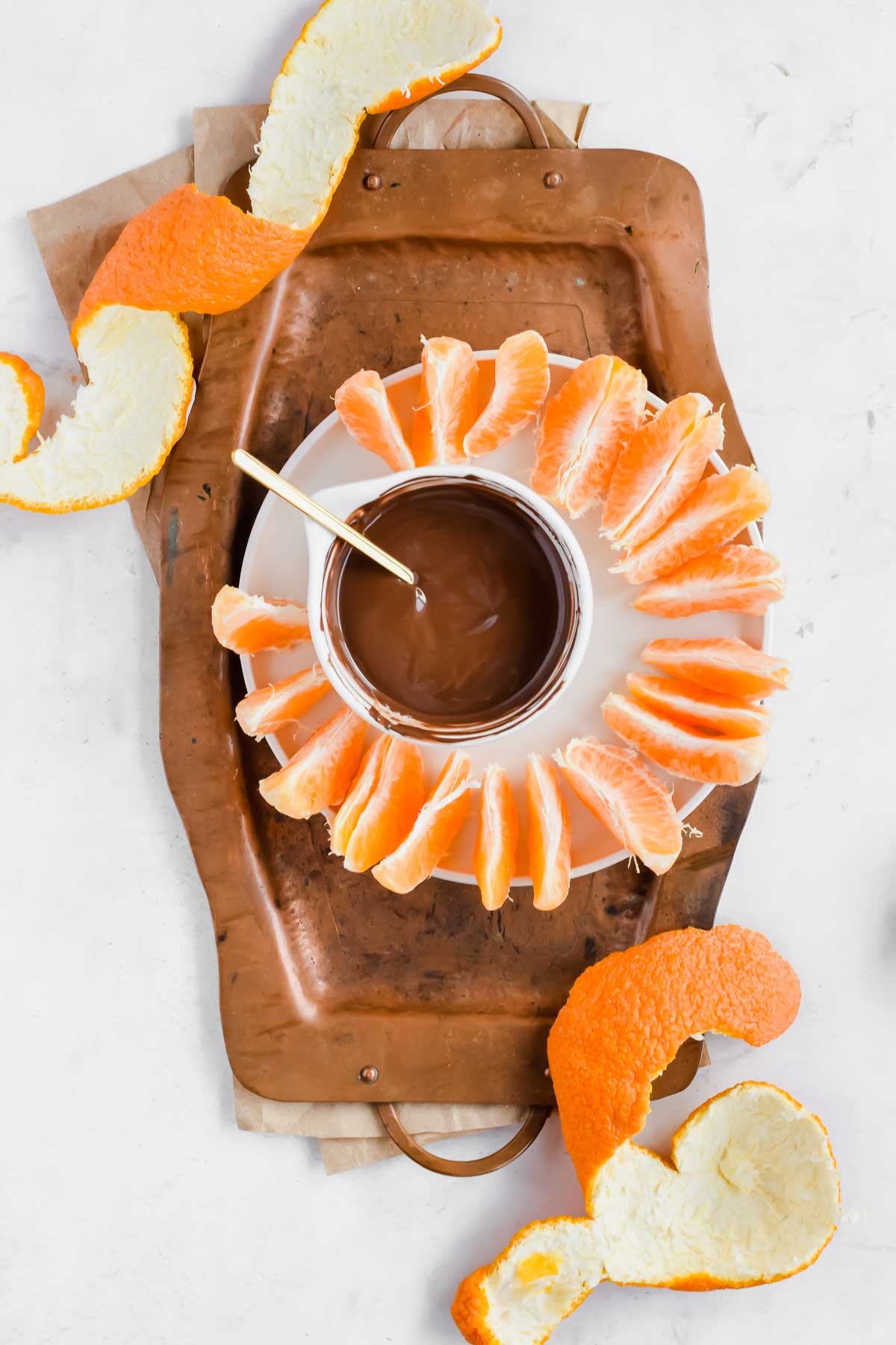 Orange slices surrounding a bowl of melted chocolate with a spoon on a plate.