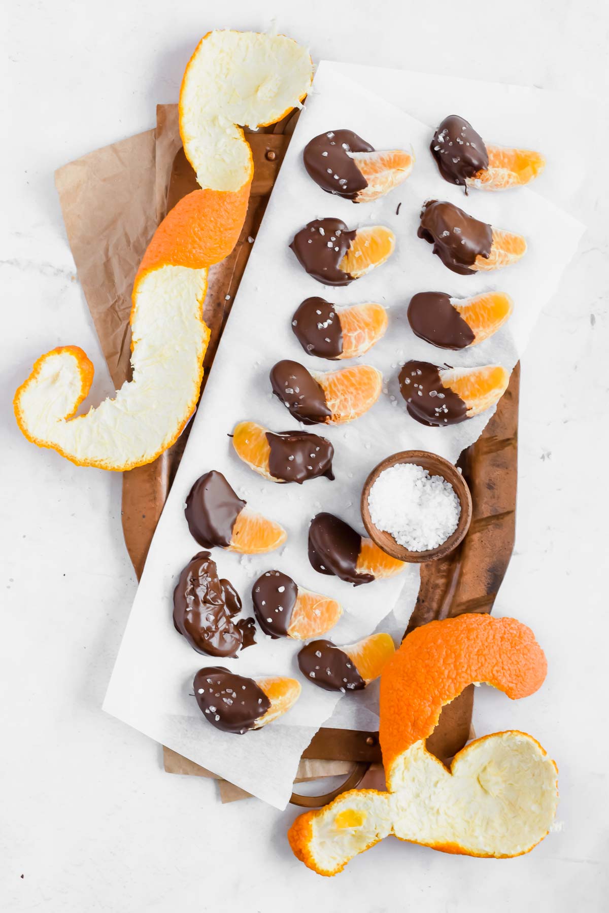 Chocolate covered oranges sprinkled with sea salt on parchment paper.