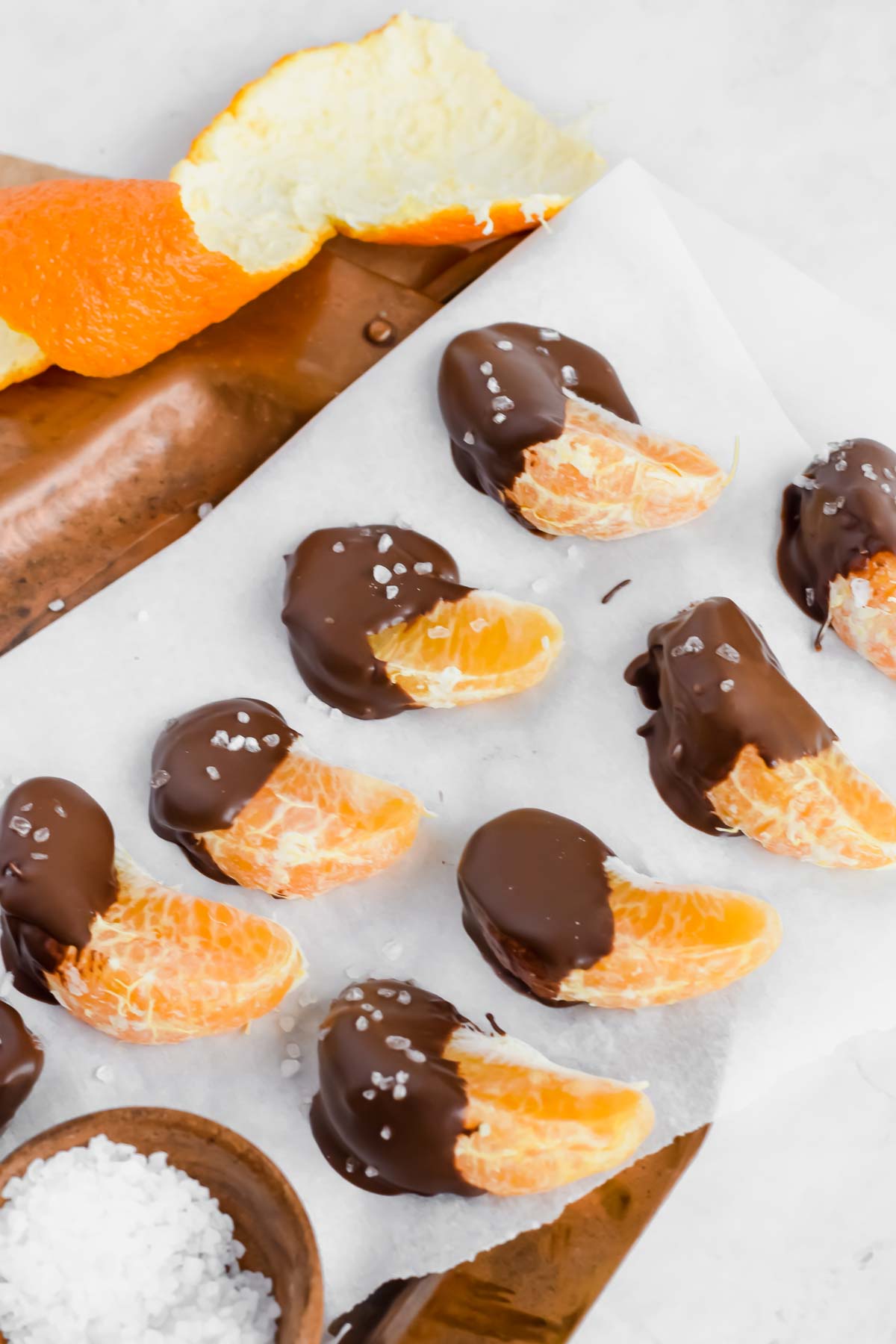 Chocolate covered oranges sprinkled with sea salt on parchment paper.
