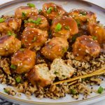 Asian chicken meatballs over bed of rice on white plate with chopsticks.