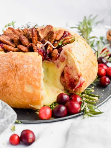 cranberry brie bread bowl with a slice removed and melty cheese flowing out.