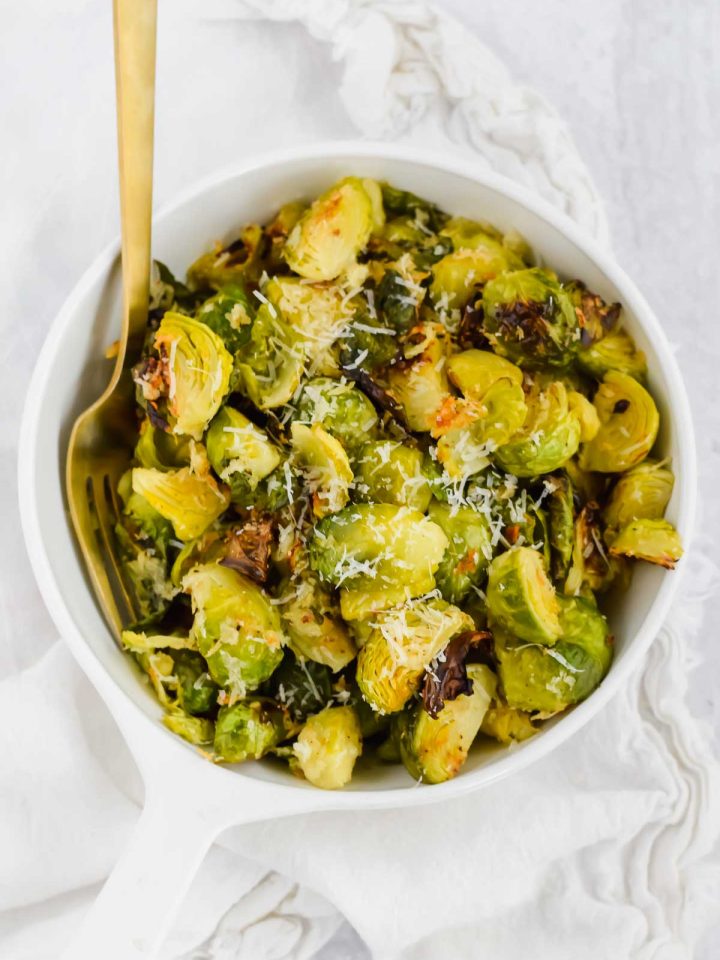 white bowl full of Crispy Parmesan Crusted Brussels Sprouts with a gold fork.