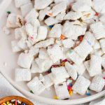 funfetti puppy chow plated on a dish beside bowl of sprinkles.